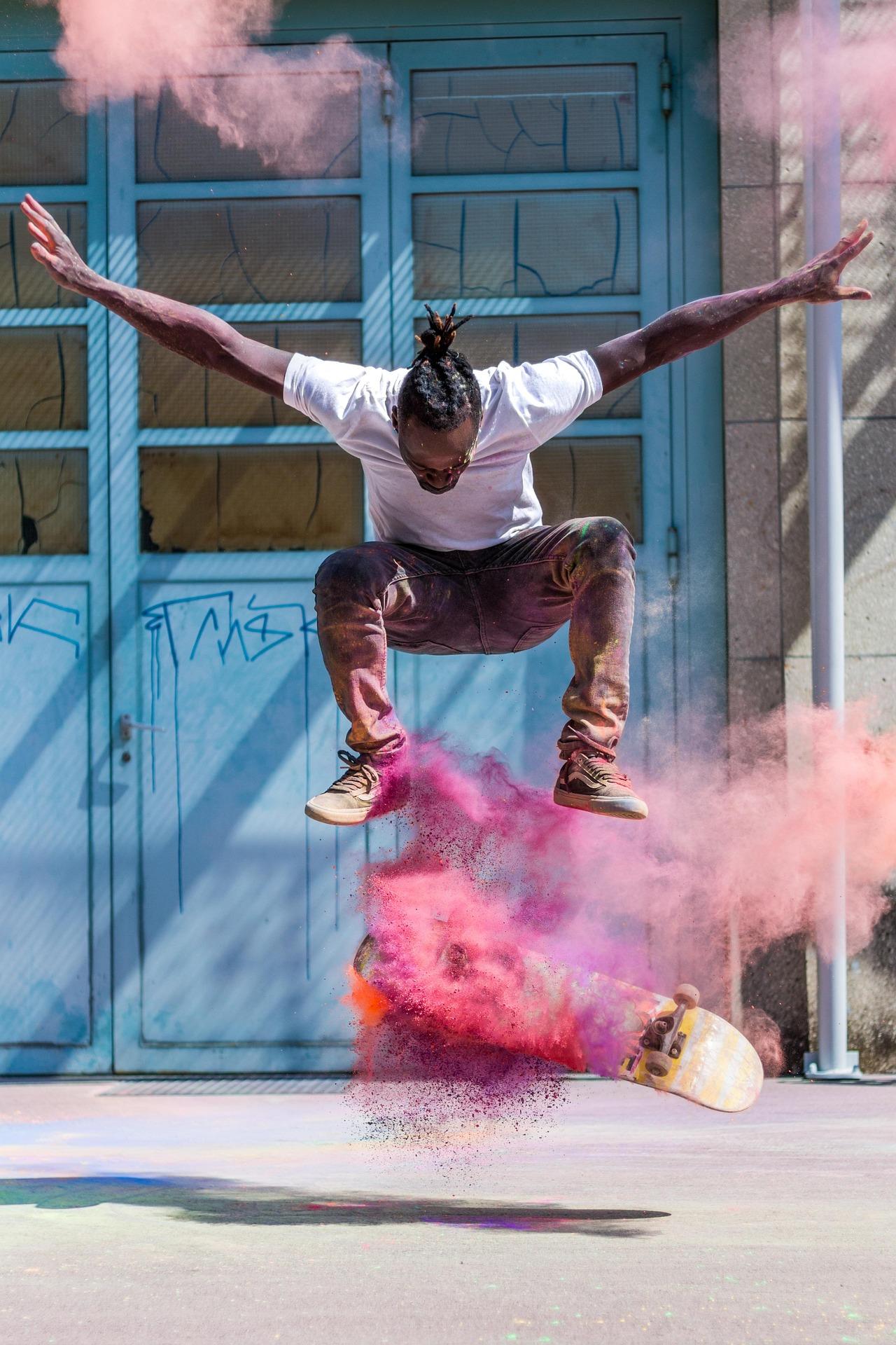 Skateboarder mid-air with flipped board as pink and purple powder bursts around the scene against blue doors.